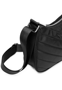 Černá nylonová taška přes rameno s prošívaným vzorem, uzávěrem na zip a nastavitelným textilním popruhem. Viditelné stříbrné kovové detaily.