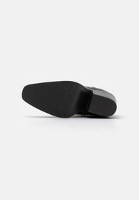Suela de zapato negra con una superficie texturizada, una punta ligeramente afilada y un talón liso. El diseño es minimalista y funcional.