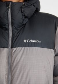 Svart og grå Columbia-jakke med glidelås foran, justerbar snorhette og en mønstret grå underdel. Har logo på brystet.