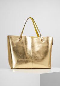 Zlatá metalická taška s hladkým, lesklým povrchem, dvěma žlutými uchy, otevřeným vrchem a bez viditelných zapínání nebo ozdob.