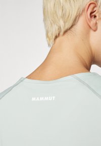 Gaiši zils sporta krekls ar apaļu apkakli, īsām piedurknēm un baltu "MAMMUT" logo aizmugurē. Gluda, viegla auduma struktūra.