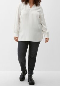 Witte lange mouwen blouse met een V-hals en geplooide manchetten, gecombineerd met donkergrijze slim-fit jeans en zwarte platform enkellaarsjes.