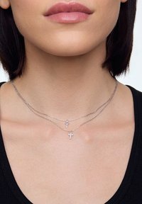 Srebrny naszyjnik warstwowy z dwiema małymi zawieszkami w kształcie krzyża. Łańcuszki są cienkie i delikatne, a jedna zawieszka jest wysadzana małymi diamentami.