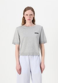 Maglietta grigia a maniche corte in maglia con scollo e orlo a coste. Presenta un piccolo etichetta nera con testo bianco sul petto.
