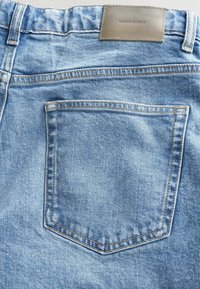 Jeans in denim azzurro chiaro con una sola tasca posteriore, cuciture gialle a contrasto e un'etichetta in pelle marrone con la scritta "DENIM SUPPLY."