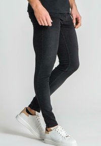 Jeans negros ajustados con una textura suave, que presentan un corte slim y detalles de costura sutiles, combinados con zapatillas blancas con acentos marrones.