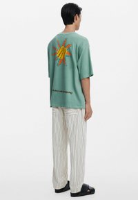 Mint green oversized t-shirt with a sun graphic in orange and yellow on the back. Paired with striped pants and black sandals.