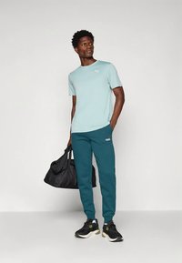 Jasnoniebieska koszulka z okrągłym dekoltem z białym logo Puma, w połączeniu z ciemnozielonymi dresami z małym logo Puma i czarnymi butami sportowymi.