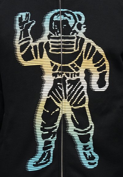 Γραφικό αστροναύτη με ριγωτή σκίαση σε αποχρώσεις μπλε και κίτρινου πάνω σε μαύρο φόντο, διαιρεμένο από ένα κεντρικό φερμουάρ.