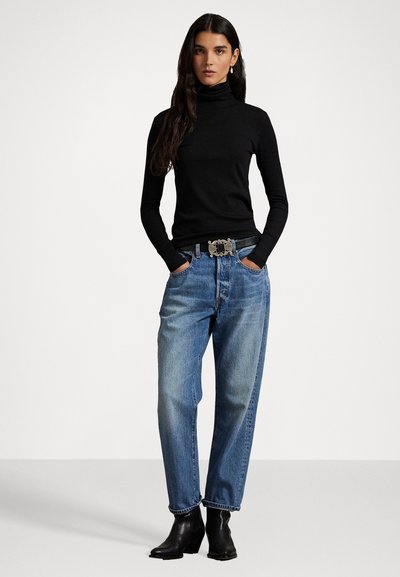 Maglione a dolcevita nero, jeans chiari a vita alta e stivali alla caviglia. La cintura presenta una fibbia decorativa in argento, con una texture liscia e una vestibilità aderente.
