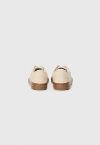 Beige kanvas sneakers med gummisåle, med lavt design, sømmen detaljer og en teksturert brun gummihæl med logo.