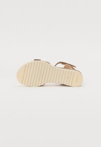 Brown suede sandal with a flat beige rubber sole, featuring a textured grip and an adjustable buckle strap for a secure fit.