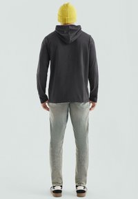 Szary sweatshirt z kapturem, żółta dzianinowa czapka, jasnoniebieskie dżinsy i czarno-białe sneakersy. Miękka faktura i casualowy design.