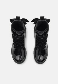 Bottines en cuir verni noir avec un bout arrondi, lacets en velours noir et doublure intérieure douce. Présente des accents de nœud assortis sur la languette.