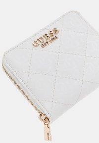 Witte gequiltte portemonnee met gouden hardware, voorzien van het "GUESS" logo in reliëf op de voorkant en een ritssluiting.