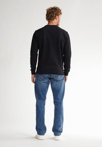 Sudadera negra de manga larga con cuello redondo y puños de canalé, combinada con jeans rectos de color azul claro y zapatillas blancas.