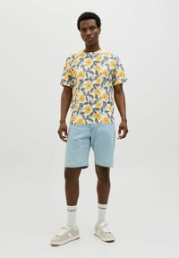 Tricou floral cu modele galbene și verzi, cu guler rotund; asortați cu pantaloni scurți din denim albastru deschis. Sneakers albi și șosete cu detalii de logo.