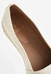 Beige espadrille-flat med en strukturerad linneöverkant och slät inredning. Har en sydd jute-kant och ett präglat varumärkeslogo på innersulan.