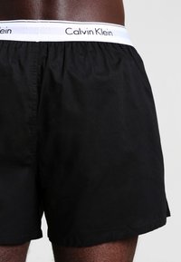Crne pamučne bokserice s elastičnom trakom na kojoj piše "Calvin Klein" bijelom bojom. Glatka tekstura, regularan kroj.