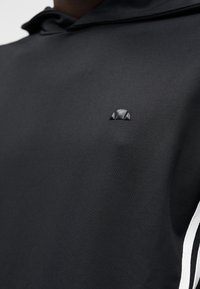 Sweatshirt com capuz preta de textura suave, com um pequeno logótipo preto no peito e riscas laterais brancas como detalhe adicional.