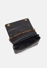 Czarna pikowana skórzana torebka z złotym łańcuszkiem, otwarta klapka odsłania puste wnętrze z markową podszewką i dwoma zatrzaskami magnetycznymi.