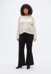 Κρεμ χρωματιστό πλεκτό τοπ με μακριά μανίκια, με κυματιστό κάτω μέρος και σχέδιο με μοτίβα. Συνδυάζεται με μαύρο, καμπανούμενο παντελόνι και μυτερά παπούτσια.