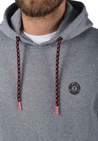 Kapuzensweatshirt aus grau gestreiftem Stoff mit einem Logo auf der Vorderseite. Verfügt über schwarze und pinkfarbene gemusterte Kordeln sowie eine strukturierte Kapuze.