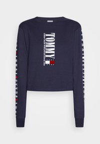 Námořnický crop top s dlouhým rukávem vyrobený z bavlny, s vertikálním bílým textem a grafikou, s dalším textem potisknutým na rukávech.