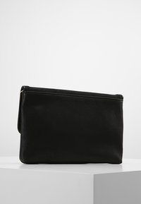 Pochette rectangulaire en cuir noir avec rabat plié, présentée sur un socle blanc sur un fond clair uni.