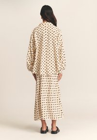 Beige polka dot shirt and skirt set, featuring a relaxed fit, long sleeves, and a smooth fabric texture. Black round buttons on the shirt.