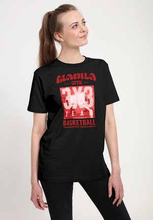 Ung kvinde med langt hestehale iført sort t-shirt med teksten "Manila City 3x3 Team Basketball Championship Tournament", kigger opad, står.