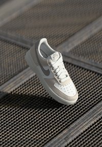 Lys grå og cremefarvede Nike Air Force 1 sneakers med en glat læderoverdel, perforeret tåboks og kontrasterende swoosh-design.