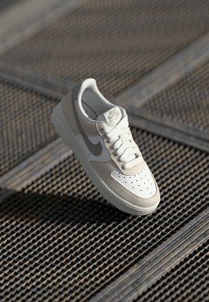 Világosszürke és krém Nike Air Force 1 tornacipők sima bőr felsőrésszel, perforált orr résszel és kontrasztos swoosh mintával.