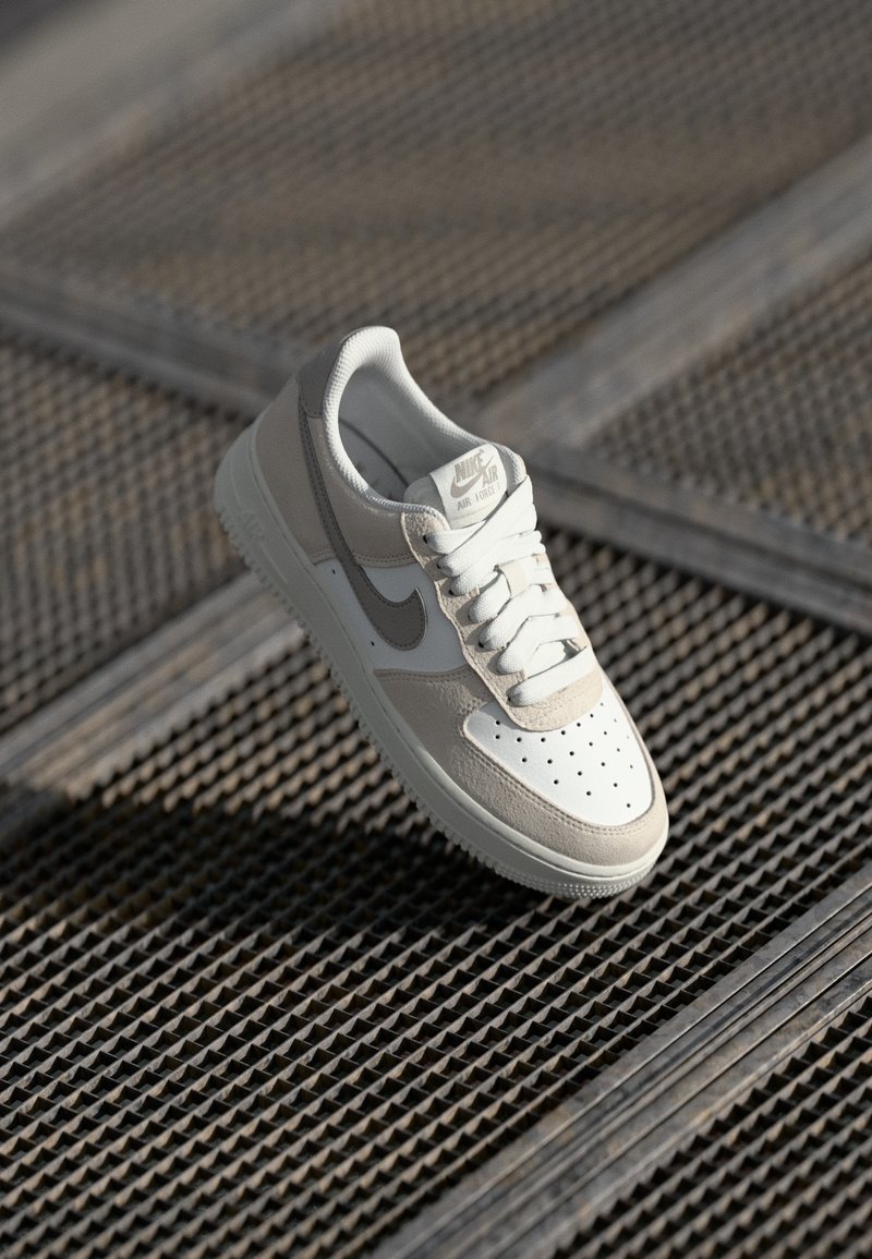 Lys grå og cremefarvede Nike Air Force 1 sneakers med en glat læderoverdel, perforeret tåboks og kontrasterende swoosh-design.