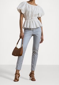 Vit broderad blus med puffärmar, åtsittande midja, matchad med ljusblå smala byxor. Brun handväska och bruna klacksandaler.