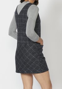 Short-sleeve gray top layered under a navy checkered dress with a textured fabric, v-neck back, and side pockets.