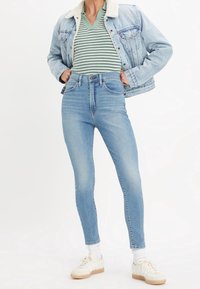 Vaqueros pitillo de tiro alto en azul claro con textura suave, combinados con una camiseta de rayas verdes y blancas y una chaqueta vaquera con cuello de borrego.