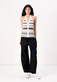 Striped halter top with a deep neckline, made of ribbed material. Paired with loose black pants, and white sneakers.