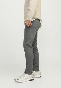 Pantalones grises de tela suave, de corte ajustado con bolsillos laterales, combinados con zapatillas deportivas plateadas que cuentan con paneles de malla y amortiguación.