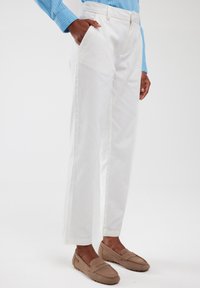 Witte katoenbroek met een rechte snit, steekzakken en een gladde textuur, gecombineerd met lichtbruine loafers.