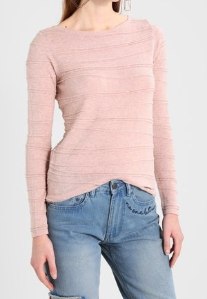 Maglietta rosa a maniche lunghe con strisce testurizzate, scollatura rotonda e vestibilità rilassata, abbinata a jeans in denim azzurro chiaro con effetto usurato.