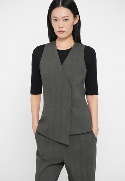 Gilet grigio senza maniche con design avvolgente, caratterizzato da un tessuto testurizzato e sottili righe verticali, abbinato a un top nero aderente e pantaloni coordinati.