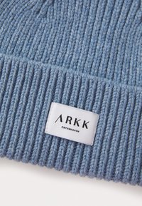 Bonnet bleu en tricot avec une texture côtelée et une étiquette blanche portant "ARKK COPENHAGEN" en texte noir.