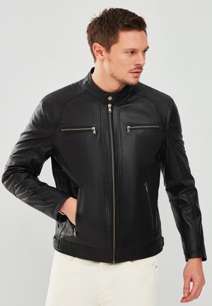 Black leather jacket with a stand collar, zippered front, and two chest pockets. Features textured details and fitted design.