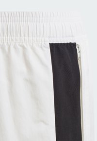 Witte shorts met zwarte zijpanelen, voorzien van een elastische tailleband en ritsdetails. Soepele stof met een contrasterende textuur van het paneel.