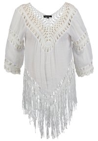 Top blanc en crochet avec col en V, manches trois-quarts, détails de dentelle complexes et longues franges pendantes à l'ourlet.