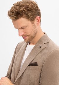 Beige pinstriped blazer made of corduroy, featuring a notch lapel, side pocket with a brown patterned handkerchief, and branded lapel pin.