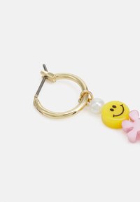 Brinco em forma de argola dourada com um bead amarelo em forma de sorriso, um bead de pérola e um bead rosa em forma de flor, com acabamento brilhante e design curvado.