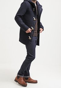 Marinblå huva rock med toggelknäppning, kontrasterande rutig foder, bärs över en brun tröja och mörk denimjeans, tillsammans med bruna stövlar.