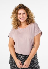 Jasnoróżowa bluzka z krótkimi rękawami i podwiniętymi mankietami, w zestawie z ciemną spódnicą w print tygrysa. Miękka faktura, luźny krój i okrągły dekolt.